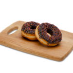 two ring doughnuts with black icing and halloween sprinkles on a wooden chopping board